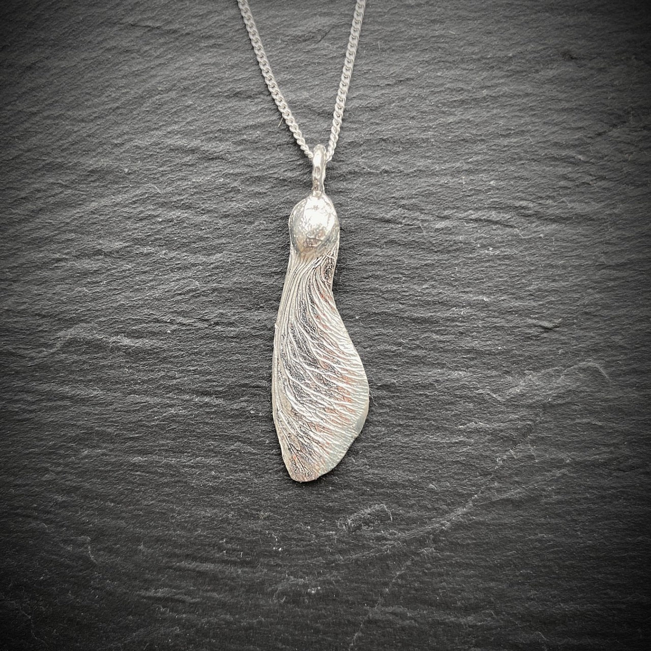 solo maple key necklace "helicopter" in silver on a slate background