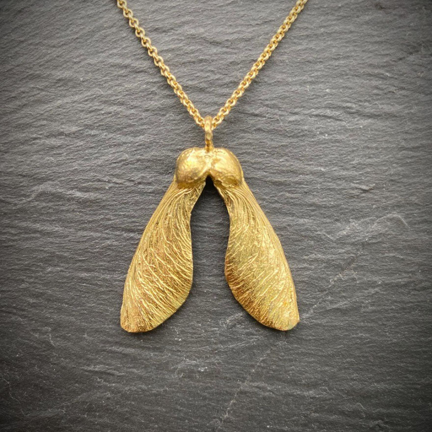 golden necklace with wonderful detail of a double maple key or "helicopter" on slate tile background