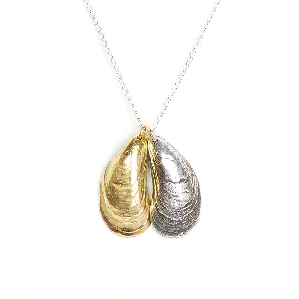 pendant comprised of two mussel shells with incredible detail that have been cast in metal: one in sterling silver the other golden. on white background.