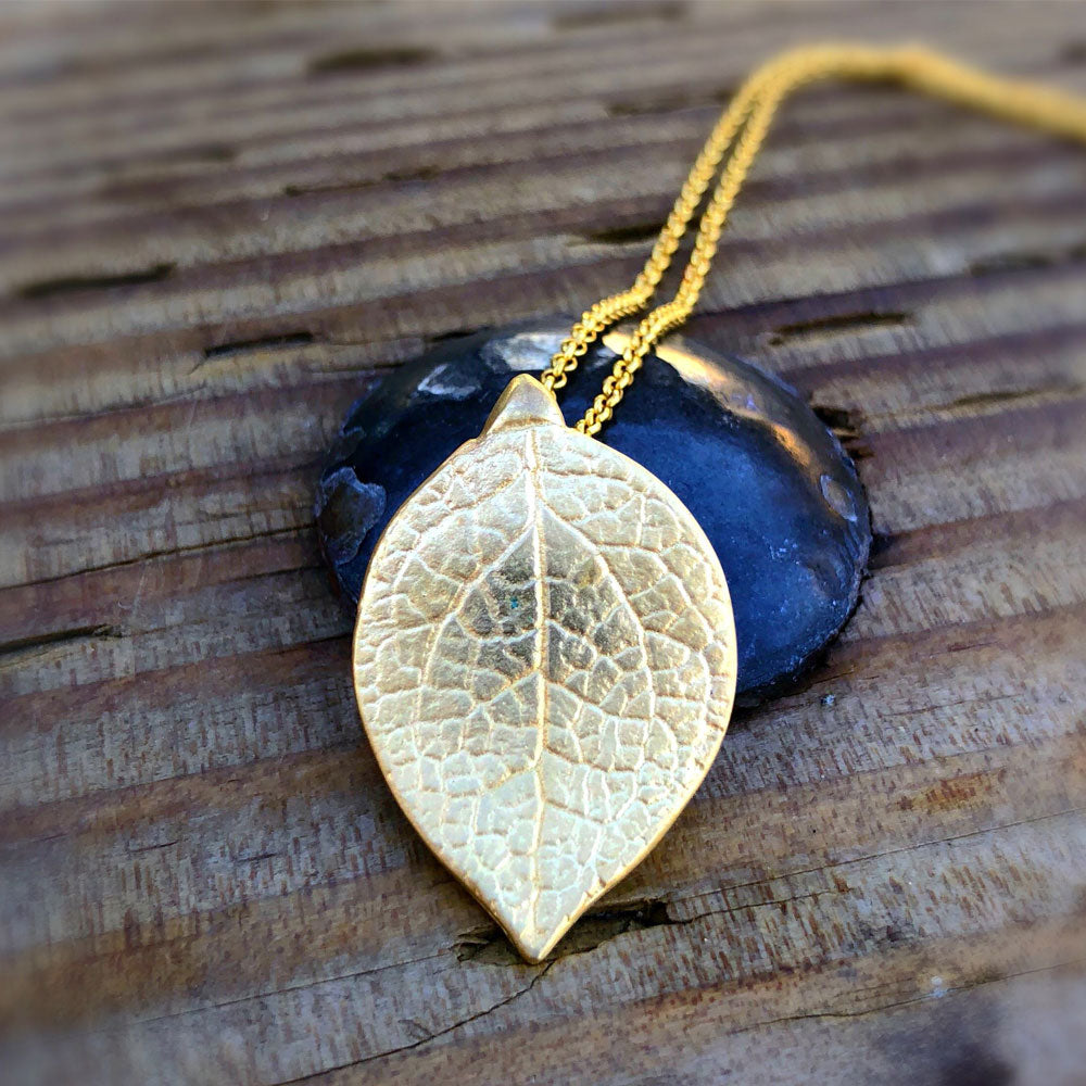 Large salal leaf necklace in golden bronze. on wood grain table with metal rivet