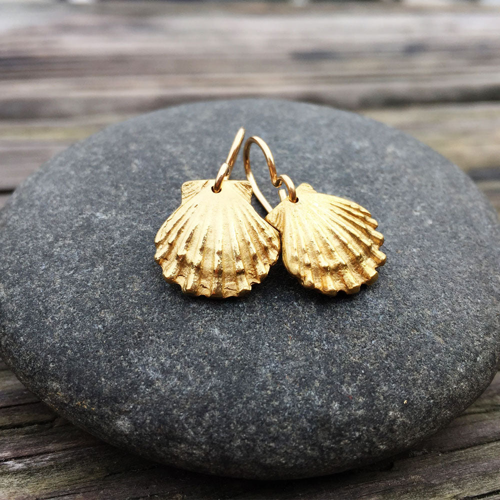 golden bronze scallop shell earrings on top of a round stone