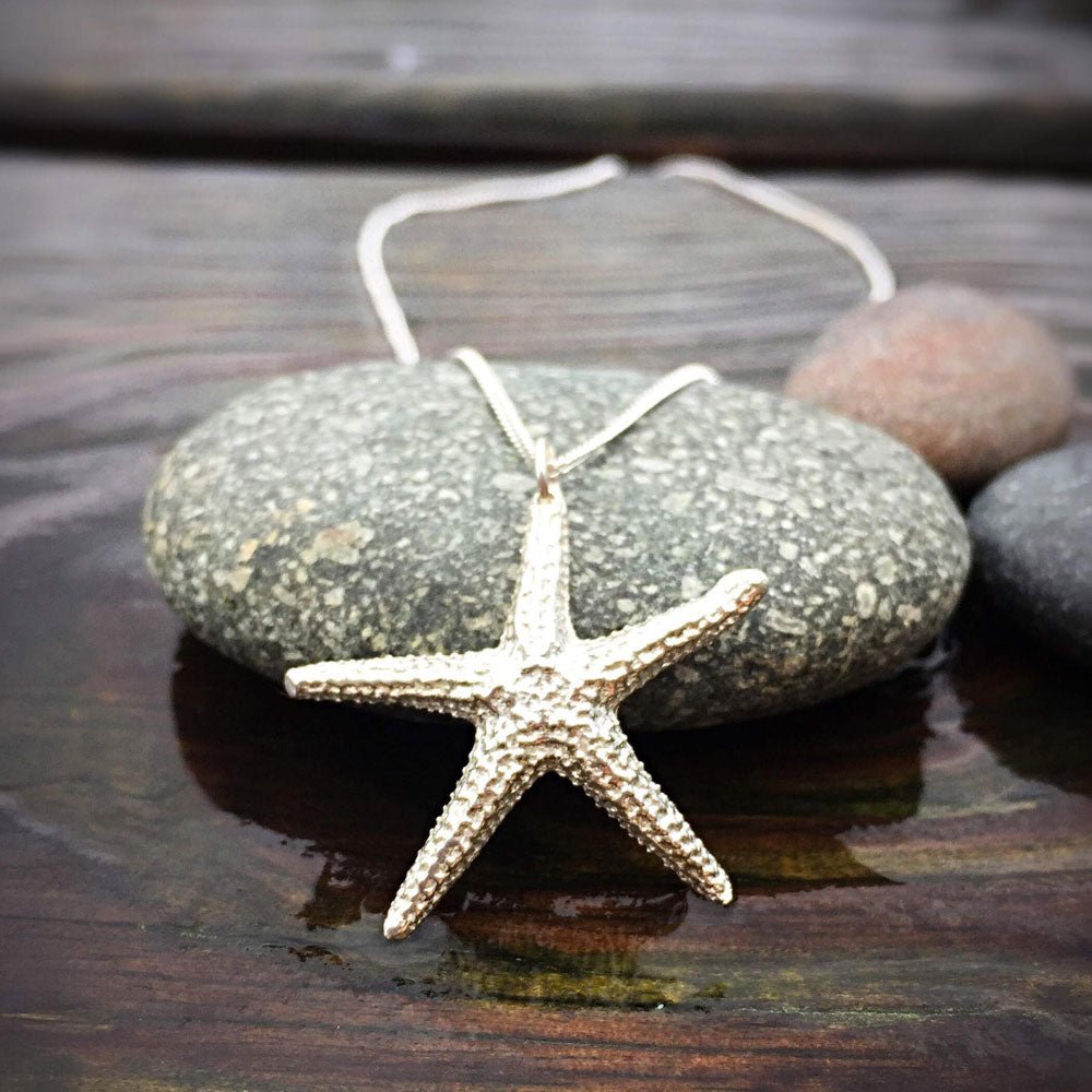 sterling silver starfish pendant perched against a round flat stone on a weathered wooden surface