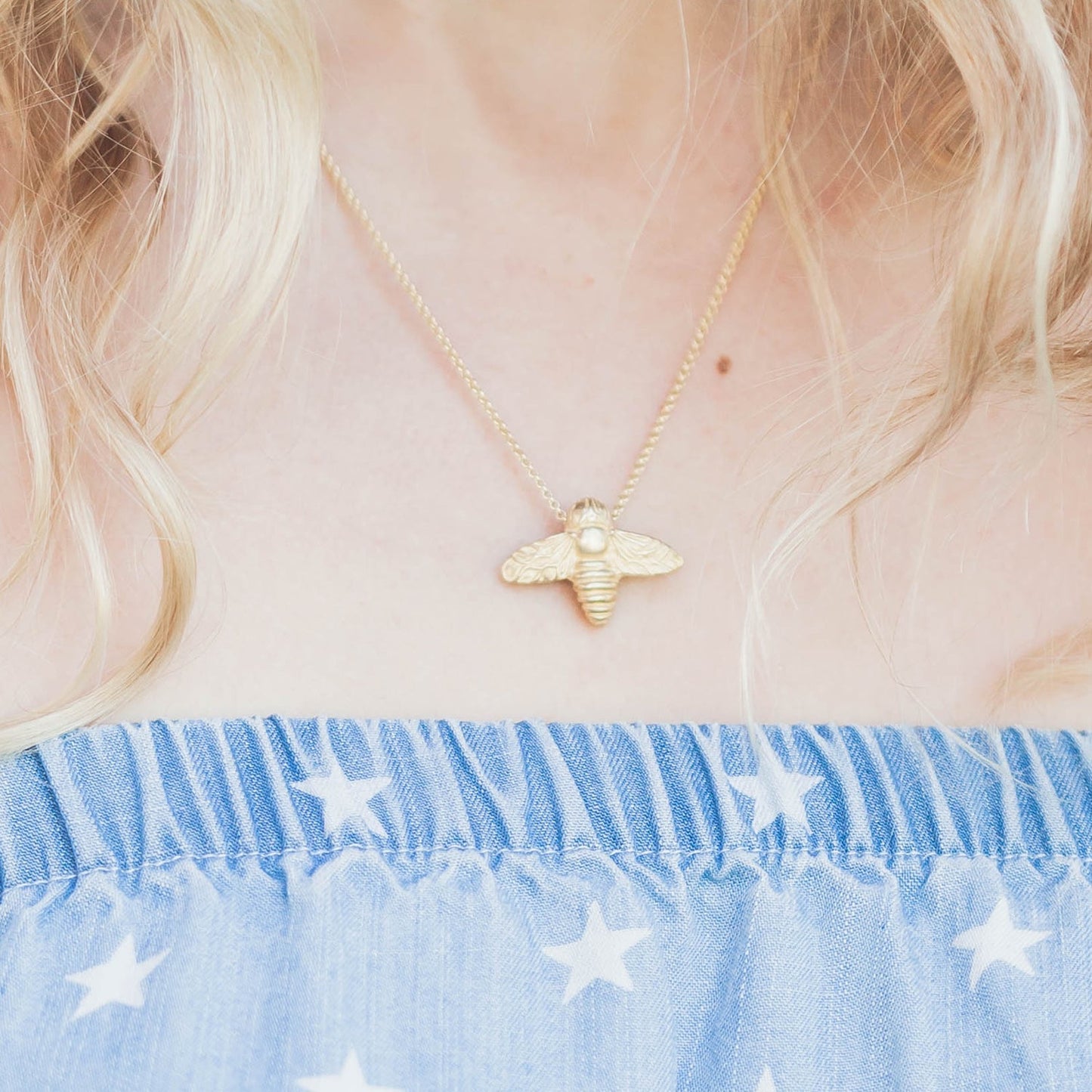 close up of a woman wearing a golden bee necklace