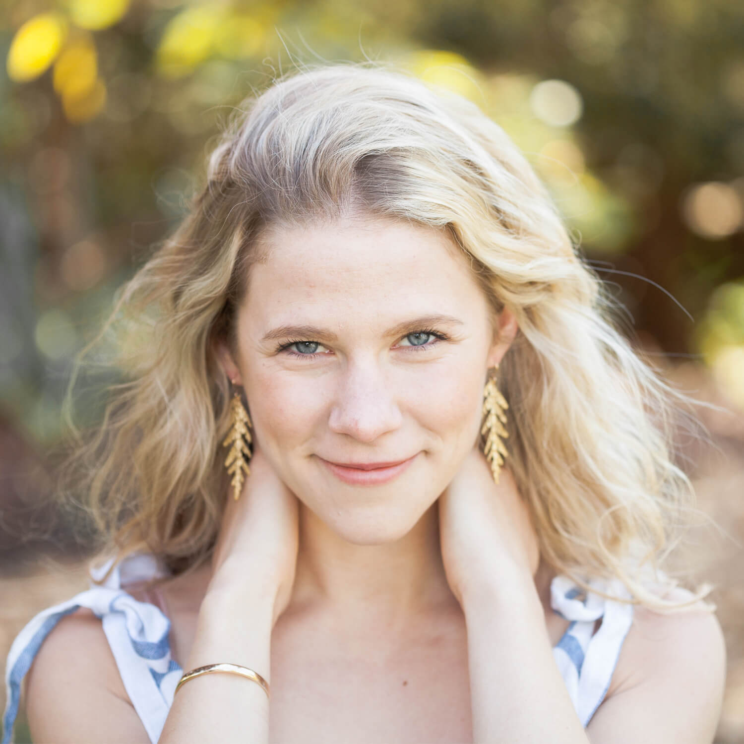 Large golden cedar leaf earrings on blond model in nature