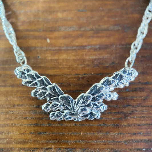 close up, detailed image of silver butterfly pendant composed of two sprigs of cedar creating the wings of the butterfly. 