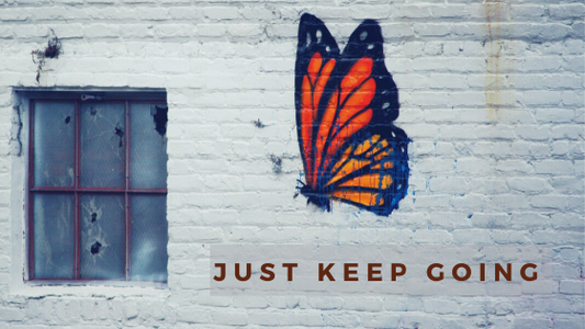 butterfly painted on white brick wall. caption: Just Keep Going