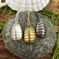 three chiton shell pendants side by side, sterling silver, golden bronze, and oxidized silver, sitting atop a round stone.