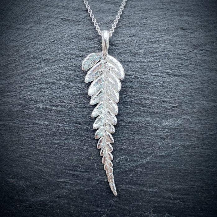 sterling silver fern leaf pendant necklace on a gray textured background