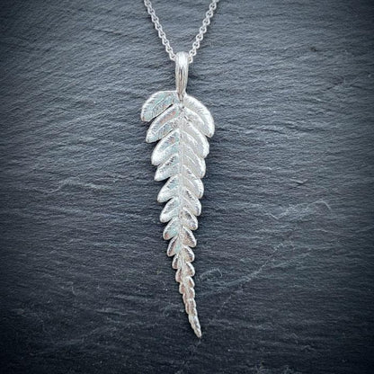 sterling silver fern leaf pendant necklace on a gray textured background
