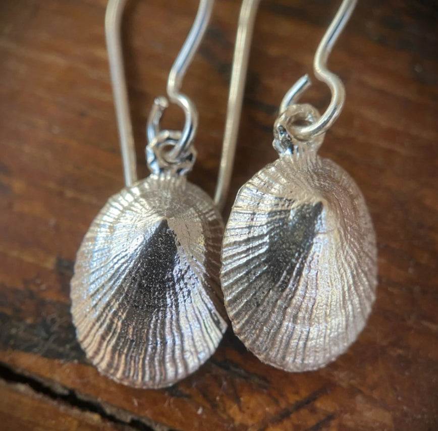 beautifully detailed pair of sterling silver limpet earrings on a wooden background