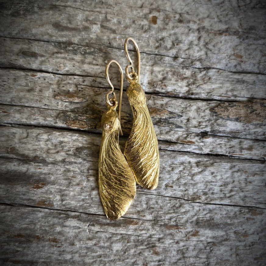 pair of solo maple key "helicopter" earrings in golden bronze. On rough wood grain background