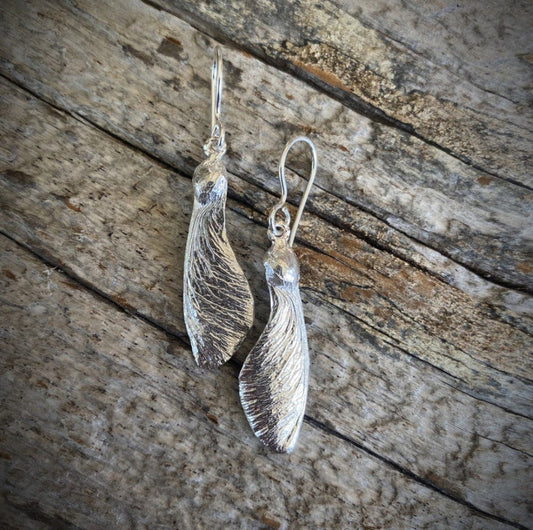 pair of solo maple key "helicopter" earrings in sterling silver. On rough wood grain background
