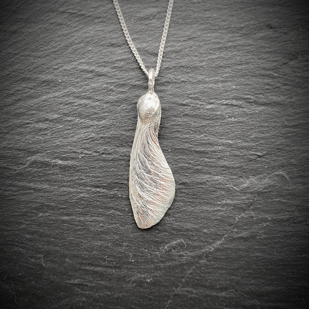 solo maple key necklace  "helicopter" in silver on a slate background