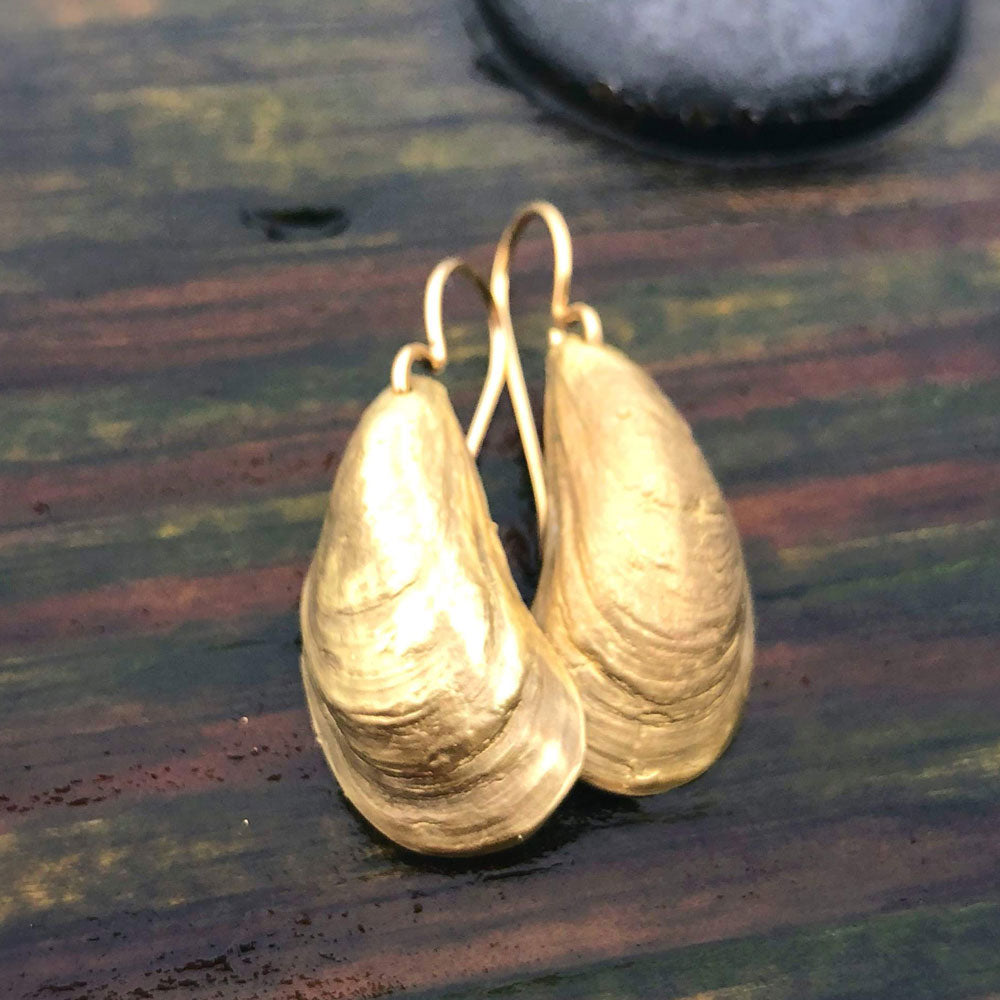 pair of golden bronze mussel shell earrings on a wood grain background