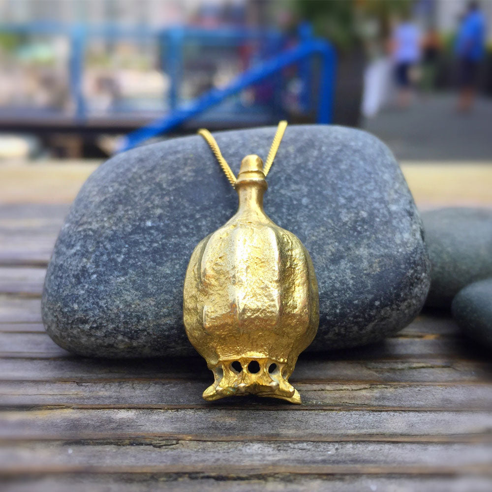 poppy pod necklace in golden bronze leaning against a rock on a wooden table top outside