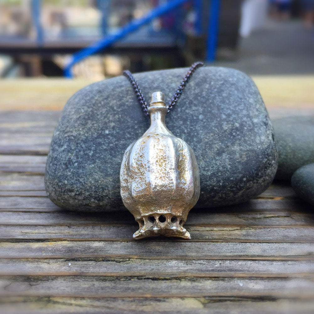 poppy pod necklace leaning against a rock on a wooden table top outside