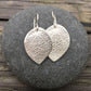 sterling silver salal leaf earrings on round grey stone with wood grain background