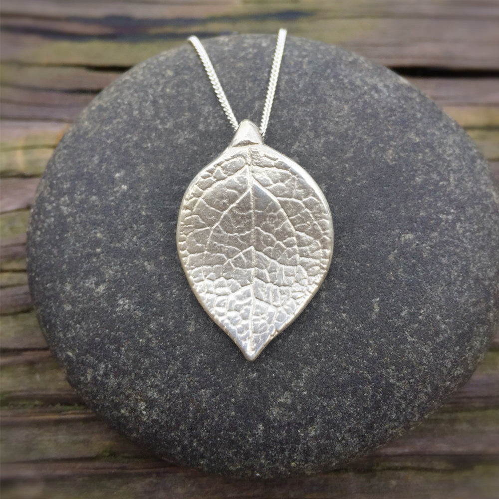 large salal leaf pendant in sterling silver. on a round grey stone on wood grain background