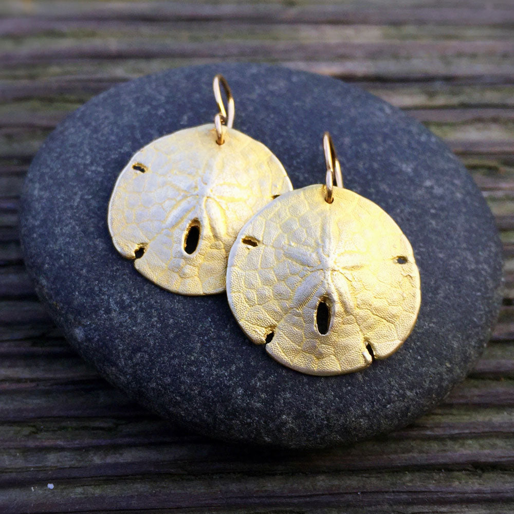 golden bronze sand dollar shell earrings on top of a round rock on a wood-grain background