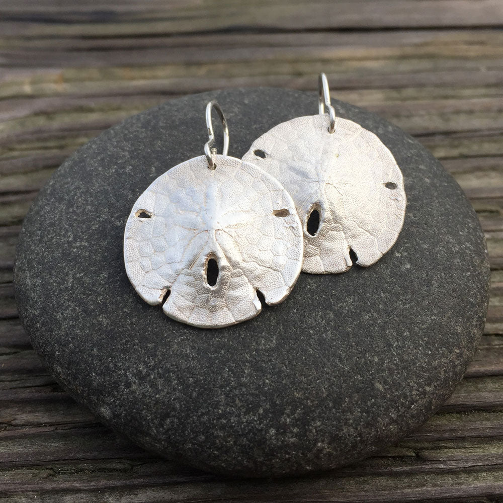 sterling silver sand dollar shell earrings on top of a round stone with a wood-grain in the background