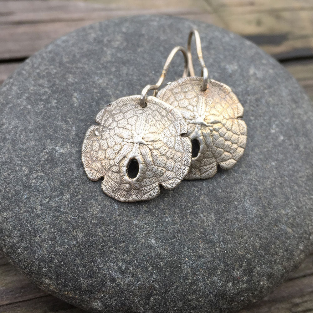 oxidized sterling silver sand dollar shell earrings sitting on top of a round stone 