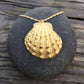 beautiful, calming image of a scallop shell cast in a golden metal on a round stone on rustic wood background