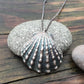 close up of beautiful, calming image of a scallop shell cast in oxidized sterling silver on a rustic wood background.
