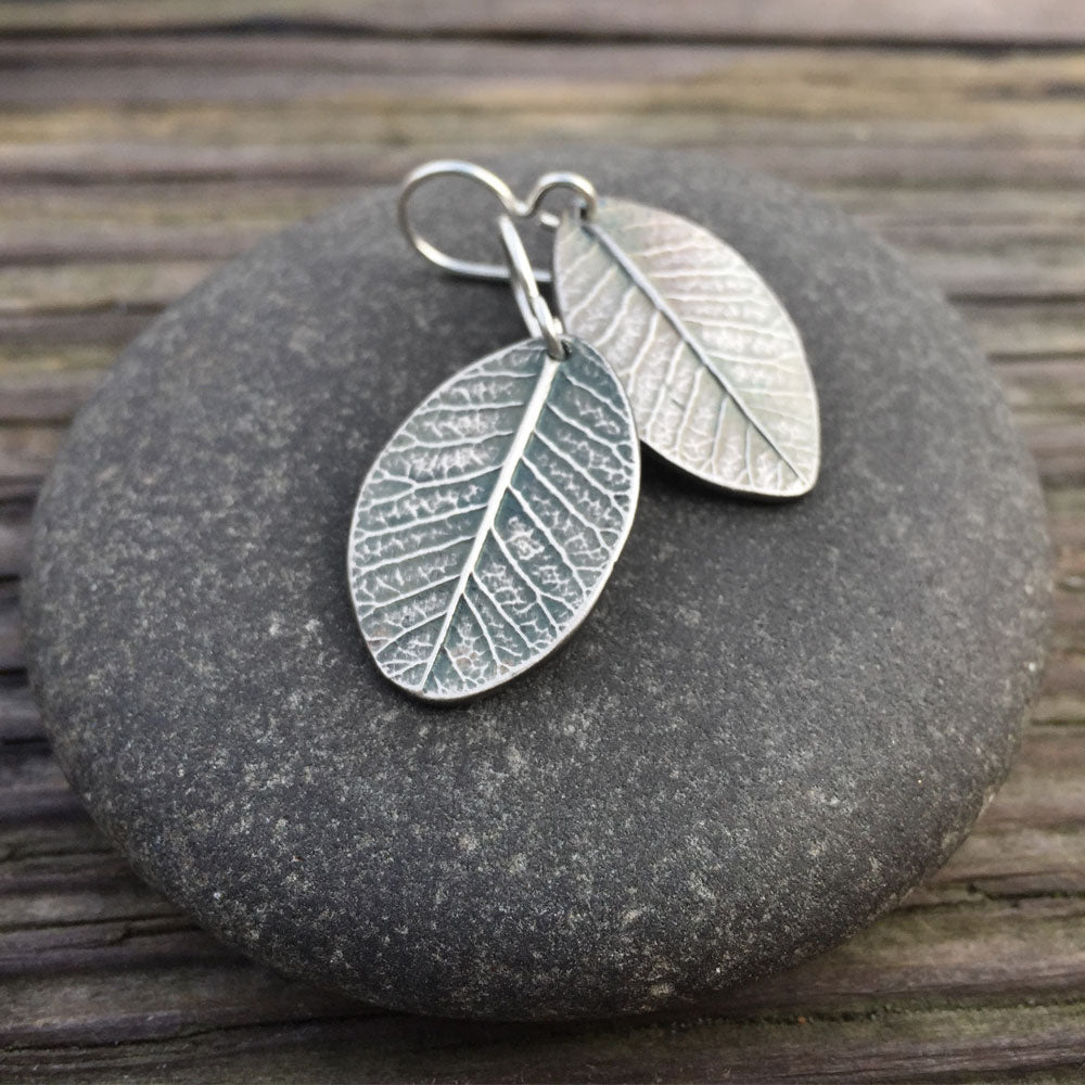 beautifully detailed oxidized sterling silver smokebush earrings on a round stone with rustic wood background