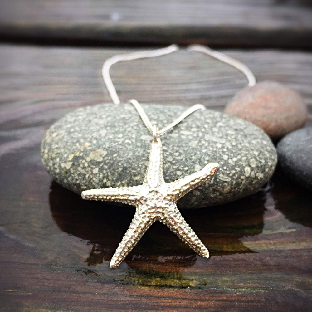 sterling silver starfish pendant perched against a round flat stone on a weathered wooden surface 
