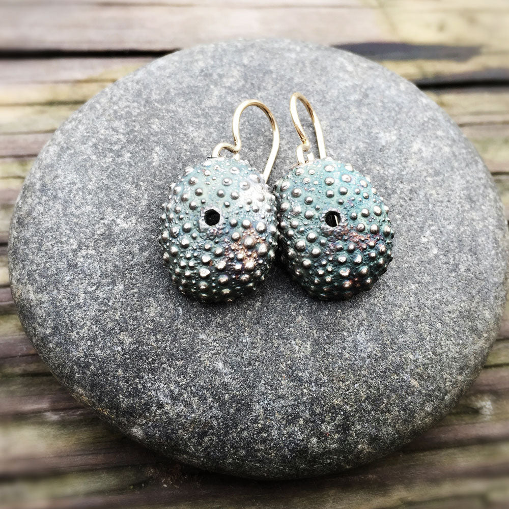 pair of beautifully detailed oxidized silver sea urchin shell earrings on a round stone with a rustic wood background