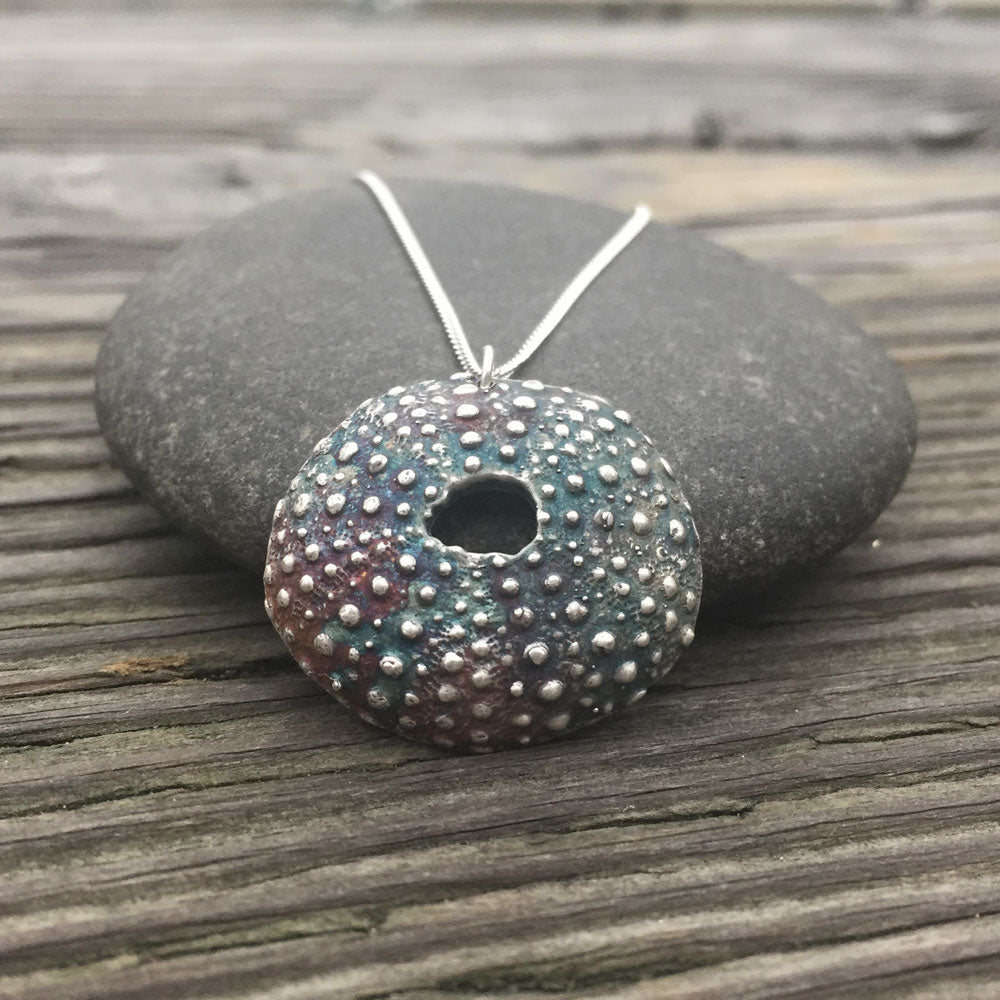 oxidized silver sea urchin necklace draped over rock on a wooden surface