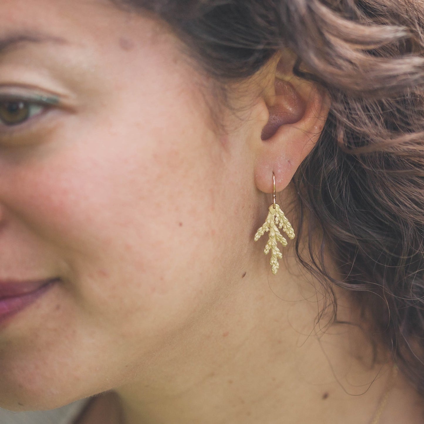 up close image of woman wearing pair of dainty gold cedar earrings