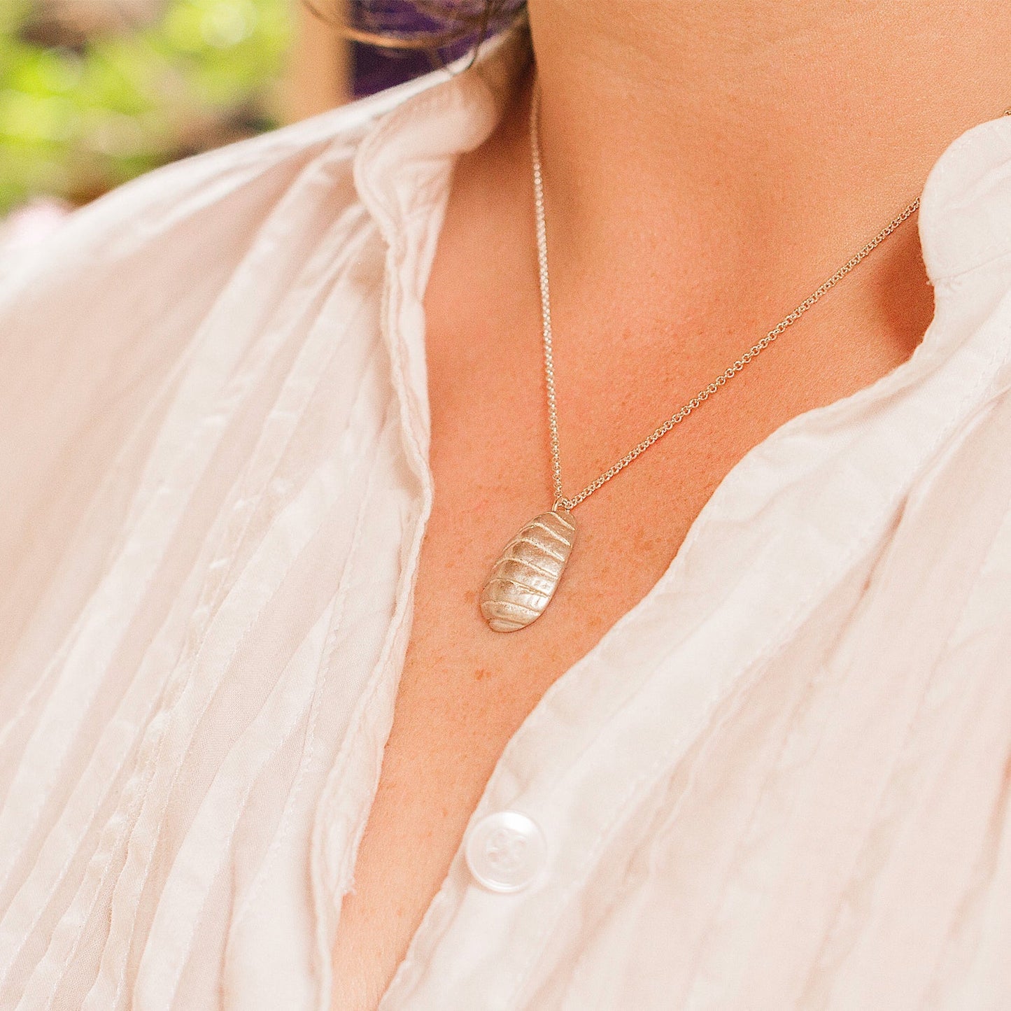 person wearing silver chiton necklace with a white, button-up top 