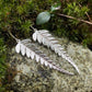 silver fern earrings sitting atop a rock surrounded by moss