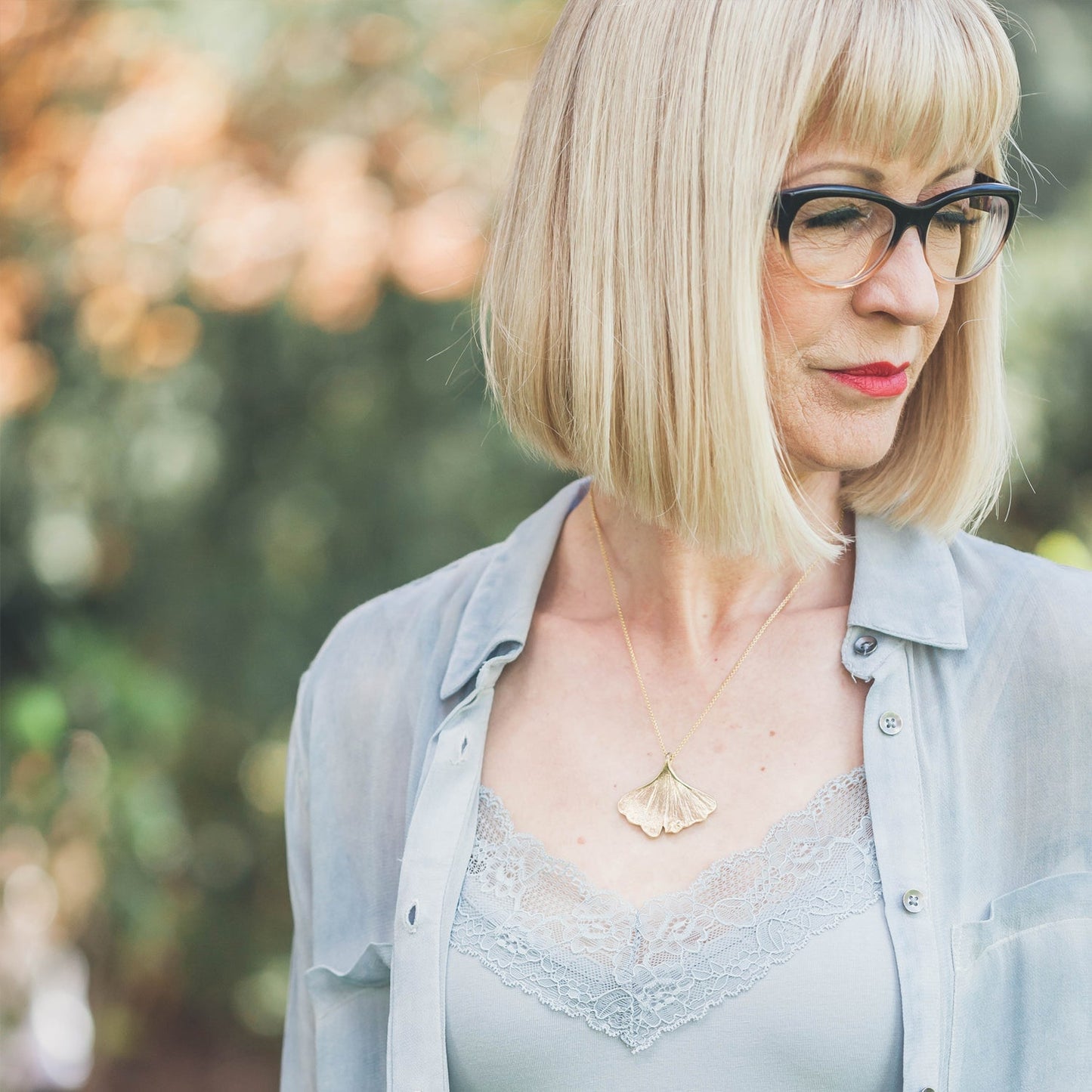 woman wearing golden ginkgo necklace with glasses and blue shirts outside