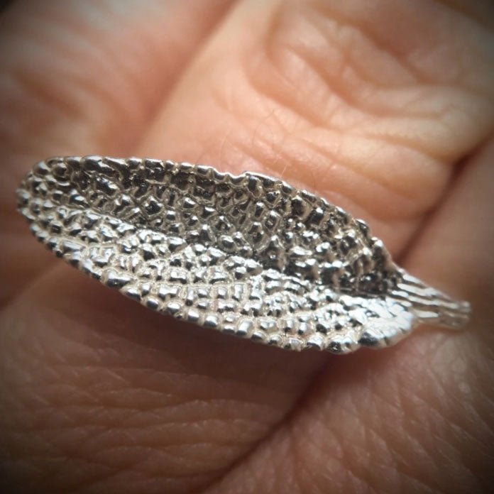 close up of sage leaf cast in sterling silver laid out horizontally as a ring displayed on a hand